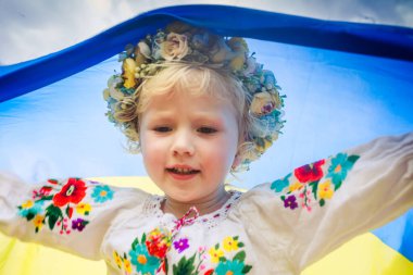 Sarı mavi Ukrayna bayrağı ezilmiş buğday tarlasında koşan kızın ellerinde. Ukrayna bayrağı taşıyan mutlu çocuk. Bağımsızlık Günü. Bayrak Günü. Anayasa Günü