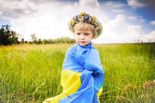 маленькая грустная украинка, завернутая в украинский флаг. ребенок с традиционным венком на голове. День независимости Украины 30 лет