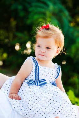 Küçük güzel kız plajda yeşil tropikal yaprakların üzerinde oturuyor. Bir çocuk seyahat ediyor. İlk kıllarında süs olan bir kız..