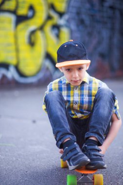 Çocuk bir kaykayın üzerinde oturuyor. Duvarlardaki duvar yazısının arka planına karşı şehirde yürüyüş yapan bir çocuk. aktif hobi, spor ve sağlık