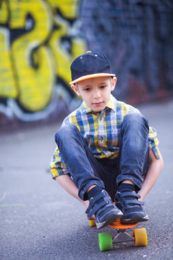 Çocuk bir kaykayın üzerinde oturuyor. Duvarlardaki duvar yazısının arka planına karşı şehirde yürüyüş yapan bir çocuk. aktif hobi, spor ve sağlık