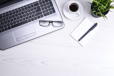 Ofis çalışma alanının en üst görüntüsü, dizüstü bilgisayarı, klavye kalemi, gözlükleri, telefonu, defteri ve kahveyi olan ahşap masa masası..