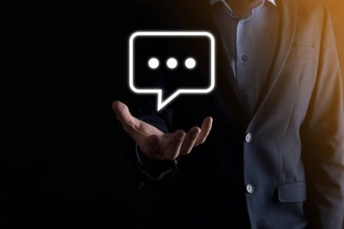 Elinde mesaj ikonu tutan bir iş adamı, elinde baloncuklu konuşma tebligat işareti var. Sohbet simgesi, SMS simgesi, yorum simgesi, konuşma baloncukları.