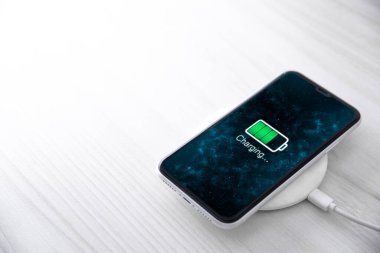 Beyaz arka planda kablosuz şarj cihazında cep telefonu var. Güç kaynağına bağlı akıllı telefonlar. Düşük pil seviyesi sorunları. Fişe takıldı