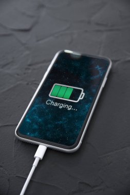 Koyu arkaplandaki kablosuz şarj cihazında cep telefonu var. Ekranda simge bataryası ve şarj süreci aydınlatması. Güç kaynağına bağlı akıllı telefonlar. Düşük pil seviyesi sorunları..