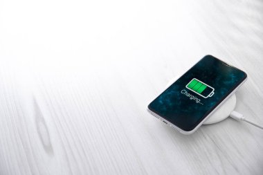 Beyaz arka planda kablosuz şarj cihazında cep telefonu var. Güç kaynağına bağlı akıllı telefonlar. Düşük pil seviyesi sorunları. Fişe takıldı