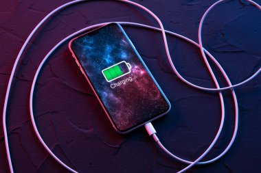 Mobil akıllı telefon kablosuz şarj cihazında koyu kırmızı ve mavi arkaplanda. Ekranda simge pili ve şarj süreci aydınlatması. Güç kaynağına bağlı akıllı telefonlar. Düşük pil.