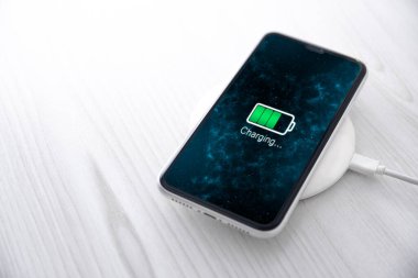 Beyaz arka planda kablosuz şarj cihazında cep telefonu var. Güç kaynağına bağlı akıllı telefonlar. Düşük pil seviyesi sorunları. Fişe takıldı