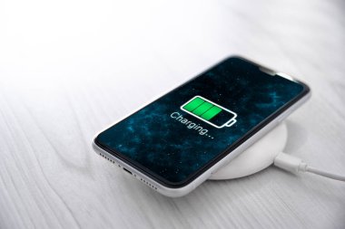 Beyaz arka planda kablosuz şarj cihazında cep telefonu var. Güç kaynağına bağlı akıllı telefonlar. Düşük pil seviyesi sorunları. Fişe takıldı