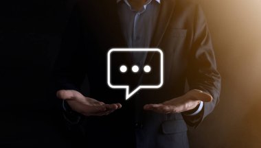 Elinde mesaj ikonu tutan bir iş adamı, elinde baloncuklu konuşma tebligat işareti var. Sohbet simgesi, SMS simgesi, yorum simgesi, konuşma baloncukları.