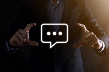 Elinde mesaj ikonu tutan bir iş adamı, elinde baloncuklu konuşma tebligat işareti var. Sohbet simgesi, SMS simgesi, yorum simgesi, konuşma baloncukları.