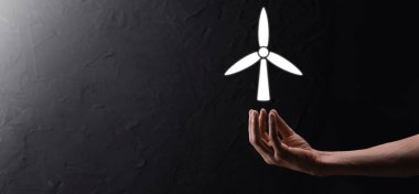 Çevresel enerji üreten bir yel değirmeni ikonu tutan bir iş adamı.