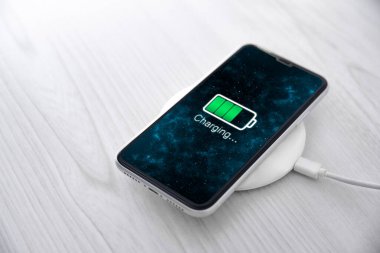 Beyaz arka planda kablosuz şarj cihazında cep telefonu var. Güç kaynağına bağlı akıllı telefonlar. Düşük pil seviyesi sorunları. Fişe takıldı