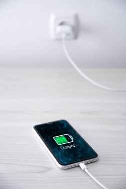 Beyaz arka planda kablosuz şarj cihazında cep telefonu var. Güç kaynağına bağlı akıllı telefonlar. Düşük pil seviyesi sorunları. Fişe takıldı