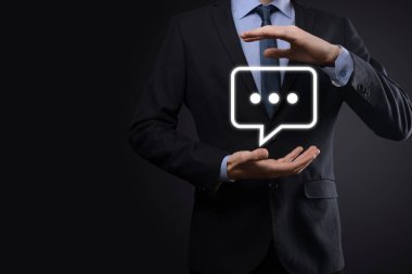 Elinde mesaj ikonu tutan bir iş adamı, elinde baloncuklu konuşma tebligat işareti var. Sohbet simgesi, SMS simgesi, yorum simgesi, konuşma baloncukları.