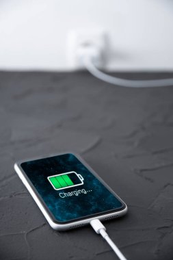 Koyu arkaplandaki kablosuz şarj cihazında cep telefonu var. Ekranda simge bataryası ve şarj süreci aydınlatması. Güç kaynağına bağlı akıllı telefonlar. Düşük pil seviyesi sorunları..