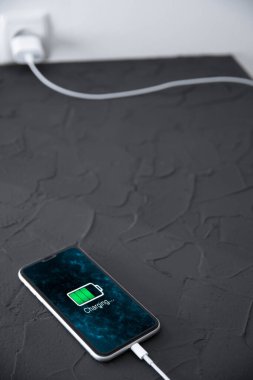 Koyu arkaplandaki kablosuz şarj cihazında cep telefonu var. Ekranda simge bataryası ve şarj süreci aydınlatması. Güç kaynağına bağlı akıllı telefonlar. Düşük pil seviyesi sorunları..