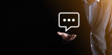 Elinde mesaj ikonu tutan bir iş adamı, elinde baloncuklu konuşma tebligat işareti var. Sohbet simgesi, SMS simgesi, yorum simgesi, konuşma baloncukları.