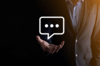 Elinde mesaj ikonu tutan bir iş adamı, elinde baloncuklu konuşma tebligat işareti var. Sohbet simgesi, SMS simgesi, yorum simgesi, konuşma baloncukları.