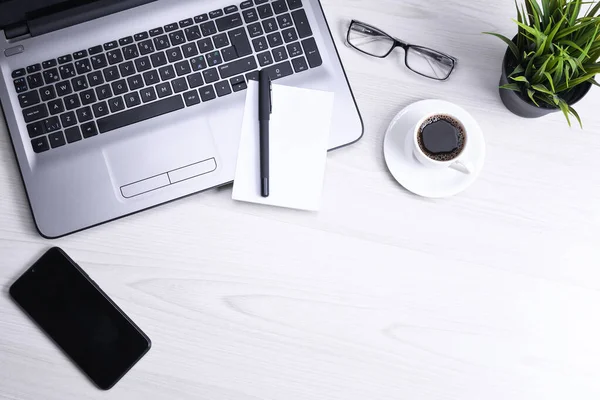 Ofis çalışma alanının en üst görüntüsü, dizüstü bilgisayarı, klavyesi, gözlükleri, telefonu ve bir fincan kahvesi olan tahta masa masası..