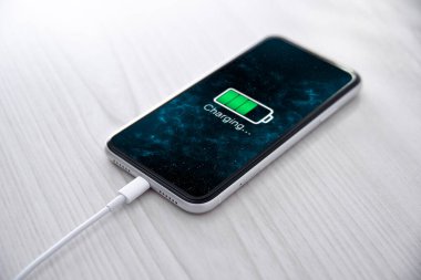 Beyaz arka planda kablosuz şarj cihazında cep telefonu var. Güç kaynağına bağlı akıllı telefonlar. Düşük pil seviyesi sorunları. Fişe takıldı