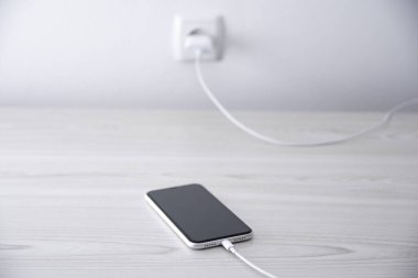 Beyaz arka planda kablosuz şarj cihazında cep telefonu var. Güç kaynağına bağlı akıllı telefonlar. Düşük pil seviyesi sorunları. Fişe takıldı