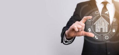 İş adamı ev ikonunu tutuyor. Marketin ev kontrollü, akıllı ev ve ev otomasyon uygulaması konsepti. PCB tasarımı ve akıllı telefonu olan kişi. Yenilik teknolojisi internet ağı kavramı