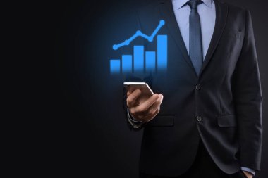 İş adamı elinde tablet tutuyor ve karanlık zemin üzerinde ok bulunan istatistik, grafik ve grafiklerin büyüyen sanal hologramını gösteriyor. Borsa. İş büyümesi, planlama ve strateji kavramı