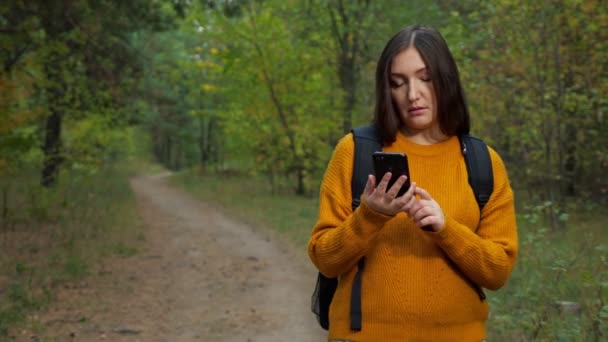 Втомлена жінка турист читає карту по телефону, що йде по лісу — стокове відео