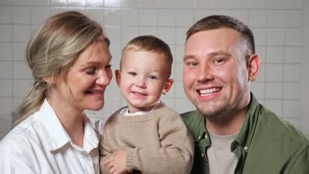 Родители держат маленького сына в руках, стоящего у стены — стоковое видео