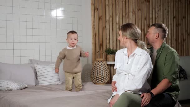 Ouders kijken naar peuter zoon springen en vallen op bed — Stockvideo