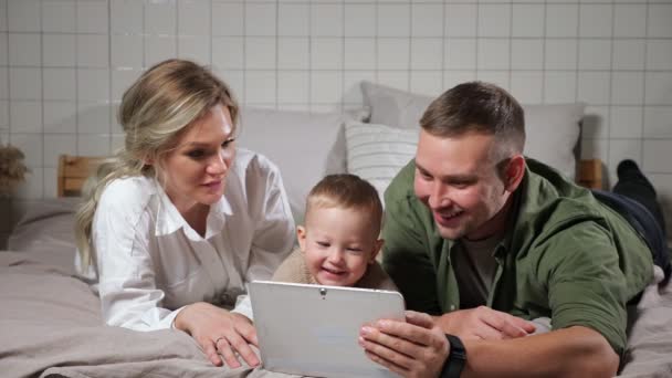Отец мать и сын смотреть учебное видео лежа на кровати — стоковое видео
