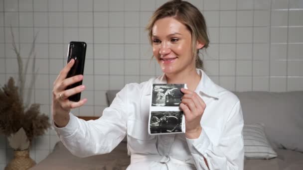 Señora embarazada muestra imagen de ultrasonido a través de videollamada — Vídeos de Stock