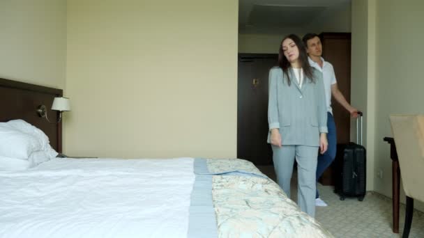Pareja joven y cansada de hombre y mujer con una maleta entra en la habitación del hotel y se cae en la cama — Vídeo de stock