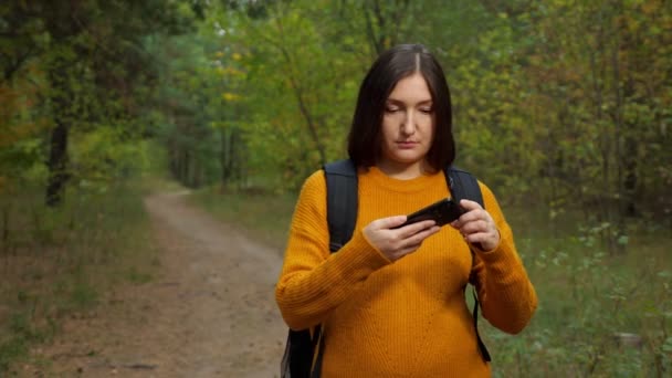 Fáradt nő turista olvas térképet telefonon séta az erdőben — Stock videók