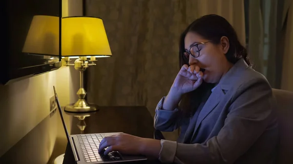Müde Frau tippt im Schein einer Tischlampe auf einem Laptop — Stockfoto