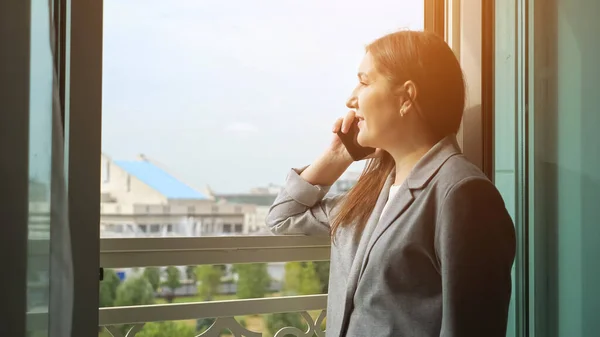 Femme en costume d'affaires parlant au téléphone près de la fenêtre ouverte par une journée ensoleillée — Photo