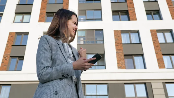 Nő egy üzleti öltöny néz a telefont, és örül a háttérben az épület, — Stock Fotó