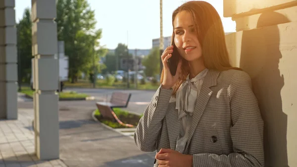 Fiatal nő egy üzleti öltönyben beszél telefonon, miközben az utcán áll — Stock Fotó