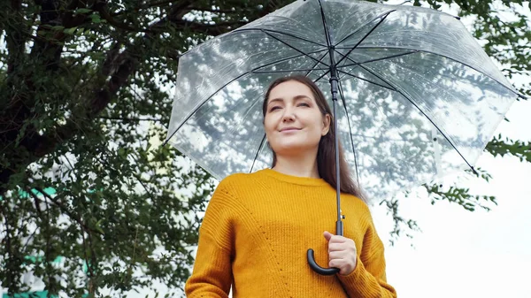 Γυναίκα σε ένα πουλόβερ μουστάρδα στέκεται κάτω από μια διαφανή ομπρέλα σε βροχερό κρύο καιρό — Φωτογραφία Αρχείου