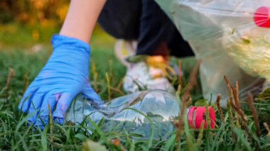 Tanımlanamayan kişi eldiven içinde çöp topluyor, geçmişi bulanık, plastik şişeyi yakın plan çekiyor.