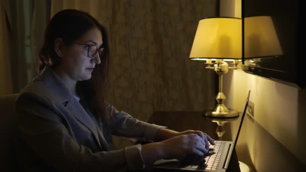 Young woman typing on a laptop under the light of a table lamp — Stock Video