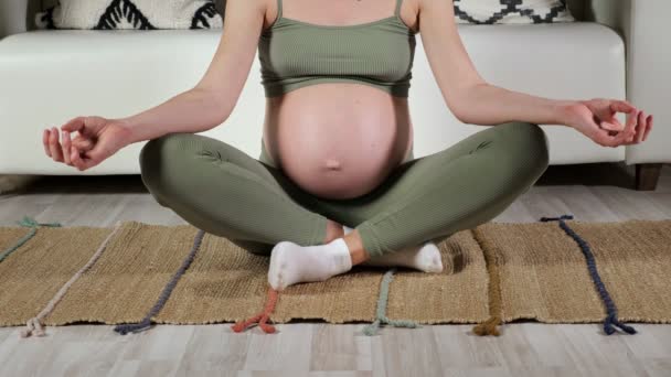 Mujer embarazada se sienta en posición de loto en la estera contra el sofá — Vídeos de Stock