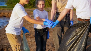 Bir ergenle birlikte dört kişi sahilde çöp topluyor. Ortak çalışma. Çevre eğitimi kavramı