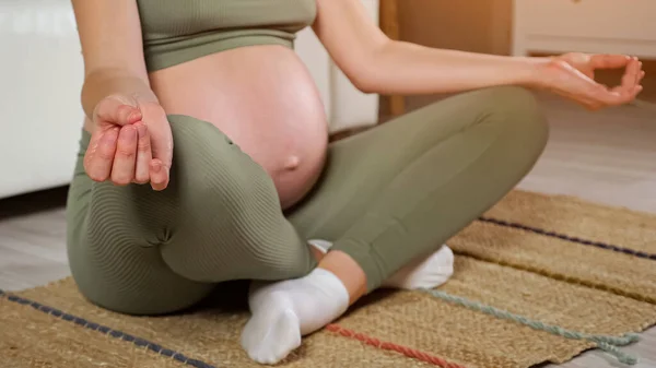 임신 한 여자는 방 안 바닥 깔개 위 로터스 위치에 앉아 있다 — 스톡 사진