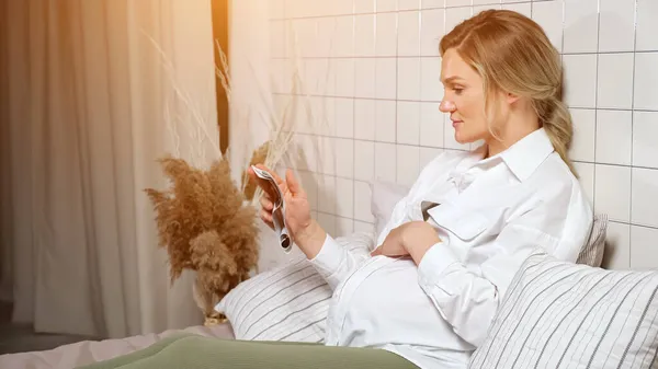 Pregnant lady strokes tummy looking at ultrasound picture — Stock Photo, Image