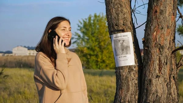 Женщина в толстовке набирает номер с постера о пропавшей собаке в парке — стоковое фото