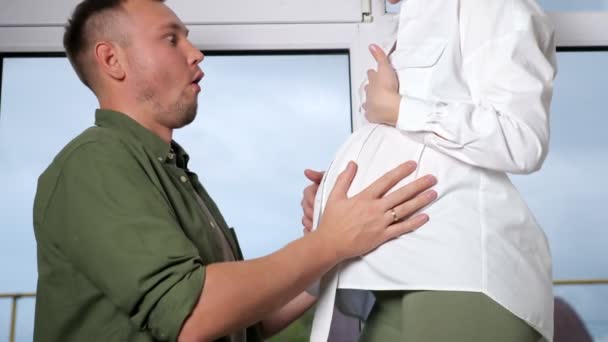 Man luistert naar kind beweegt leunend op zwangere dame buik — Stockvideo