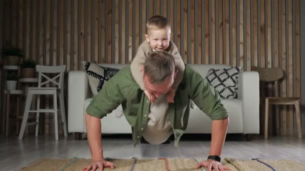 Pai empurra-se com o pequeno filho nas costas e posa olhando — Vídeo de Stock