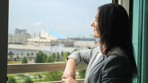 Jeune femme en costume d'affaires se tient près d'une fenêtre ouverte et regarde au loin — Photo